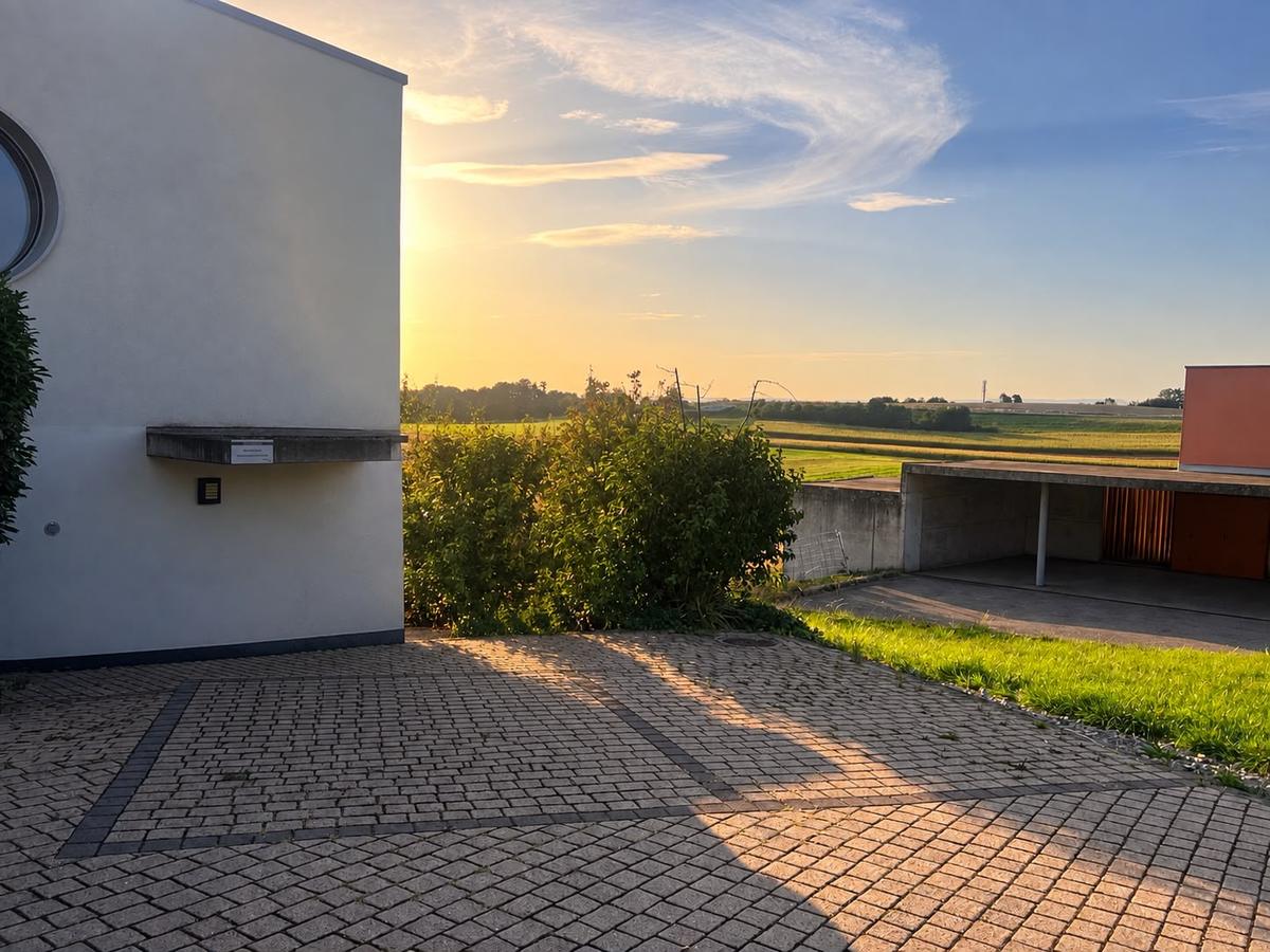 Le cabinet au coucher du soleil, avec les places de parc devant l'entrée et la campagne fribourgeoise